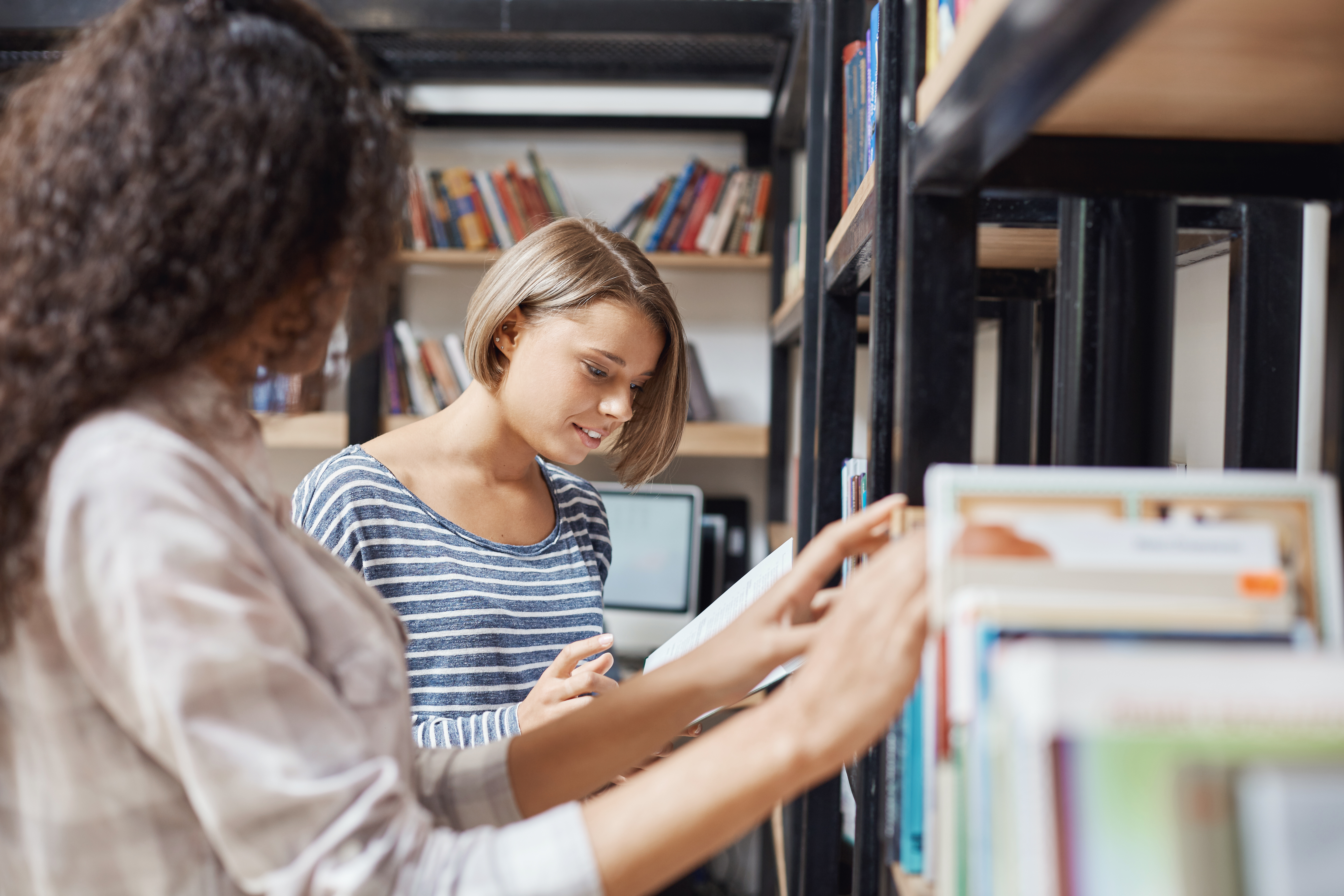 deux femmes cherchent et regardent des livres debout devant une bibliothèque